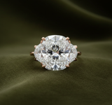 Rose gold three-stone ring with oval center and pentagon sides on dark olive green velvet