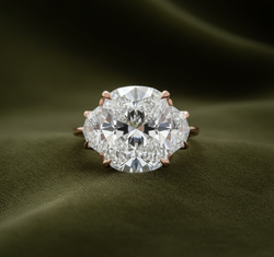 Rose gold three-stone ring with oval center and pentagon sides on dark olive green velvet